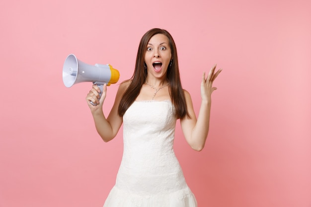 Retrato de mujer emocionada con la boca abierta en vestido blanco sosteniendo megáfono, extendiendo las manos