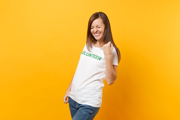 Retrato de mujer emocionada llena de alegría feliz en camiseta blanca con voluntario de título verde inscripción escrita aislado sobre fondo amarillo. Ayuda de asistencia gratuita voluntaria, concepto de trabajo de gracia de caridad.