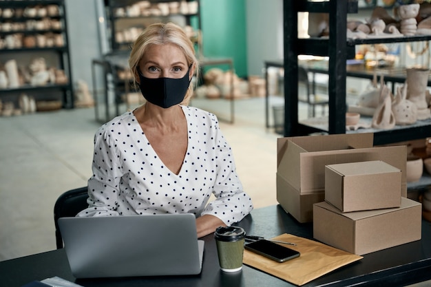 Retrato de mujer empresaria o propietaria de un negocio con mascarilla protectora usando laptop