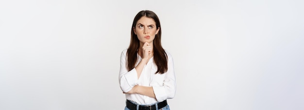 Foto retrato de mujer empresaria pensando en hacer elecciones de pie pensativo fondo blanco de estudio