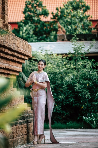 Retrato de mujer encantadora asiática vistiendo un hermoso vestido típico tailandés identidad cultura de Tailandia en el templo antiguo o lugar famoso con pose graciosamente