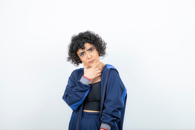 Retrato de una mujer encantadora con el pelo rizado posando contra la pared blanca.