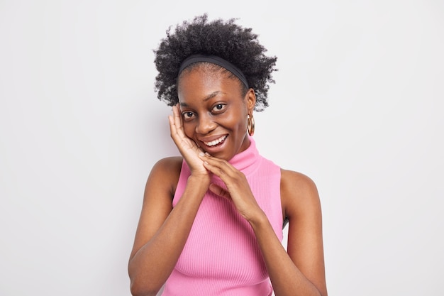 Retrato de mujer encantadora de piel oscura con belleza natural mantiene las manos cerca de la cara mira suavemente a la cámara