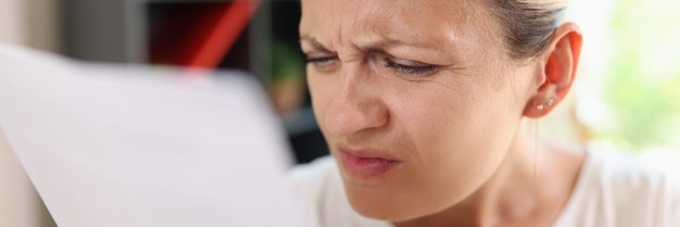 Retrato de una mujer enfocada tratando de leer periódicos entrecejando los ojos para ver más claramente a una mujer que tiene