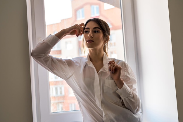 Retrato de mujer europea elegante en ropa casual mirando por la ventana y disfrutando de un clima soleado