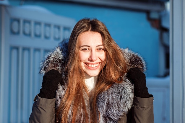 Foto retrato de una mujer europea de pelo bastante largo en un día soleado de invierno frente al fondo de la cerca azul