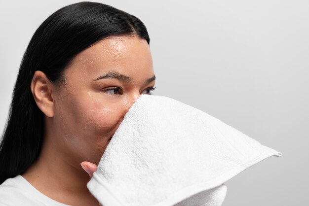 Foto retrato de mujer exfoliando la cara con producto y toalla