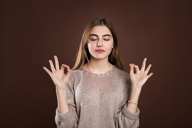 Retrato mujer con expresión tranquila y relajada, de pie en pose de yoga con brazos extendidos y signos zen sobre pared marrón. La niña se siente aliviada después de la meditación matutina