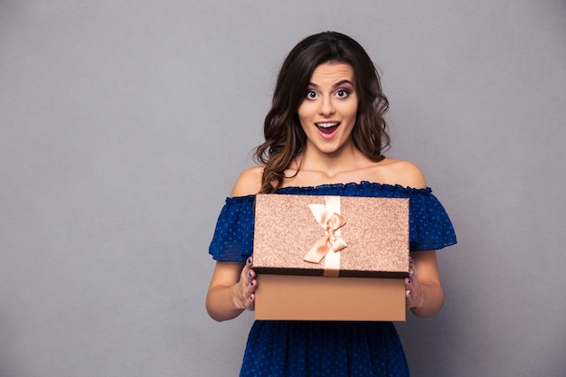 Retrato de una mujer feliz abriendo caja de regalo y sobre pared gris