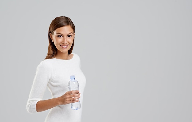 Foto retrato de mujer feliz y agua potable en estudio aislada en un fondo blanco espacio de maqueta para el bienestar botella de cara y persona con líquido para la hidratación nutrición y dieta saludable para el cuerpo