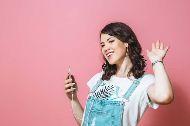 Retrato de mujer feliz con auriculares cantando aislado sobre pared rosa