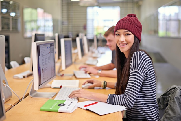 Retrato de mujer feliz y biblioteca con computadora en la universidad para aprendizaje o proyecto de educación Beca en línea y estudiante en el escritorio para navegar por el conocimiento de Internet o trabajar en una tarea