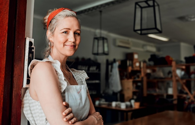 Retrato de mujer feliz y brazos cruzados por la entrada en la confianza de la pequeña empresa para el taller en la tienda minorista Diseñadora o propietaria de cerámica de mujer segura sonriendo para la artesanía o el inicio creativo