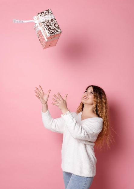 Retrato de una mujer feliz con una caja de regalo y mirando a una cámara aislada en un fondo rosa
