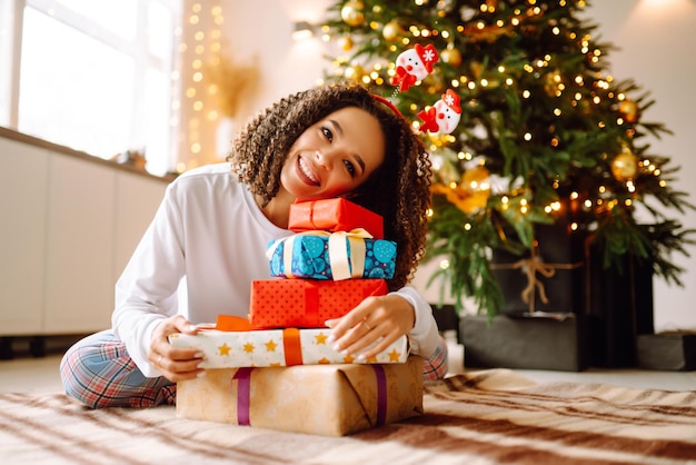 Retrato de mujer feliz celebrando las vacaciones de invierno con grandes cajas de regalo cerca del árbol de Navidad