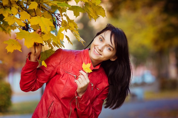 Retrato de una mujer feliz en una chaqueta de cuero roja en otoño con un arce amarillo