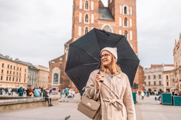 Retrato de una mujer feliz con un elegante abrigo bajo un paraguas respirando en la calle de y