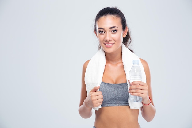 Retrato de una mujer feliz fitness con una toalla sosteniendo una botella con agua aislado en una pared blanca