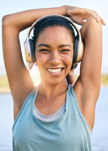Retrato de mujer feliz haciendo estiramientos de calentamiento usando auriculares para escuchar música y hacer ejercicio al aire libre Atleta femenina sonriente preparando el cuerpo y los músculos para entrenar o hacer ejercicio cardiovascular