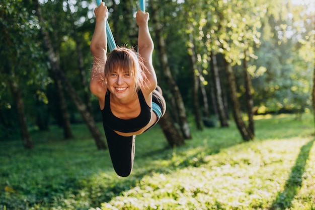 Retrato de mujer feliz haciendo fly yoga en el árbol y mirando a la cámara.