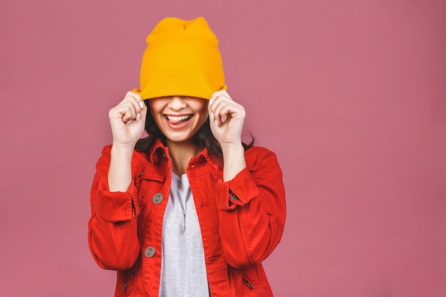 Retrato de mujer feliz joven inconformista en sombrero amarillo y camisa roja aislado sobre pared rosa.