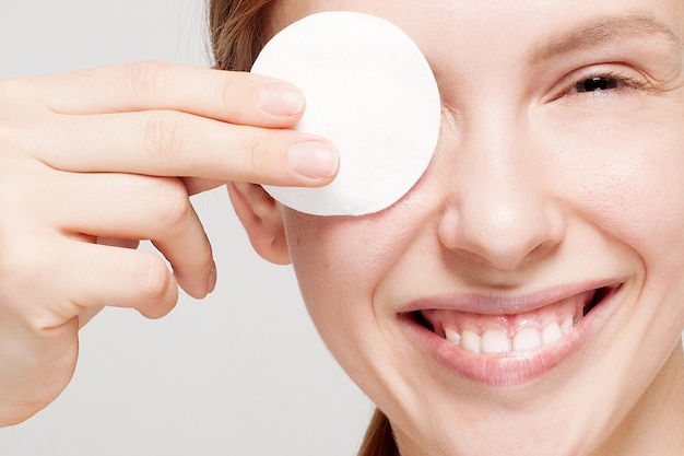 Retrato de una mujer feliz limpiando su rostro con algodones