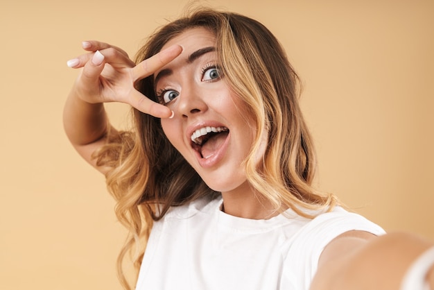 Retrato de mujer feliz mostrando el signo de la paz con los dedos mientras toma selfie foto aislada