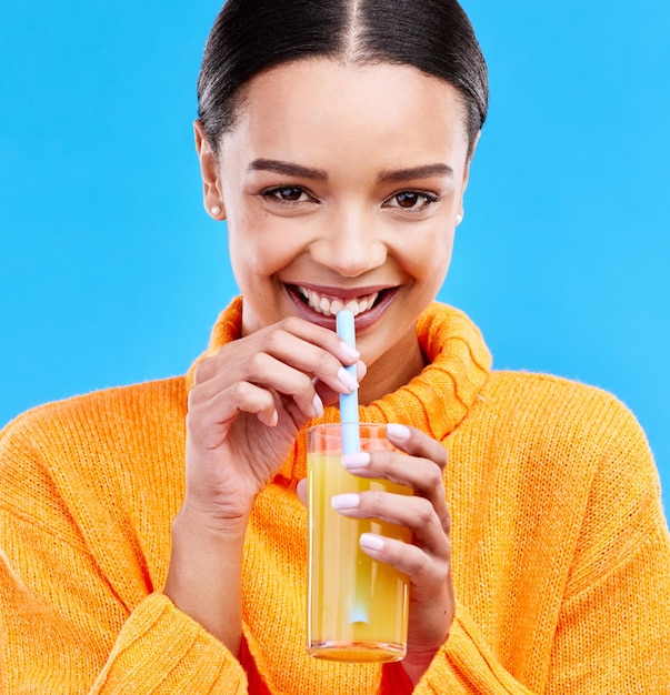 Retrato de mujer feliz y pajita para beber jugo de naranja en el fondo azul del estudio y sonrisa Vidrio de modelo femenino y sorbo de cóctel de frutas para nutrición dieta de vitamina c y batido vegano de desintoxicación