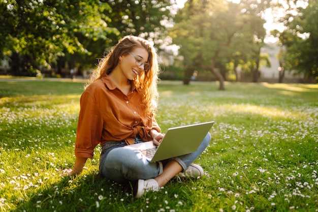 Retrato de una mujer feliz en un parque soleado en un césped verde con una tecnología de concepto independiente portátil