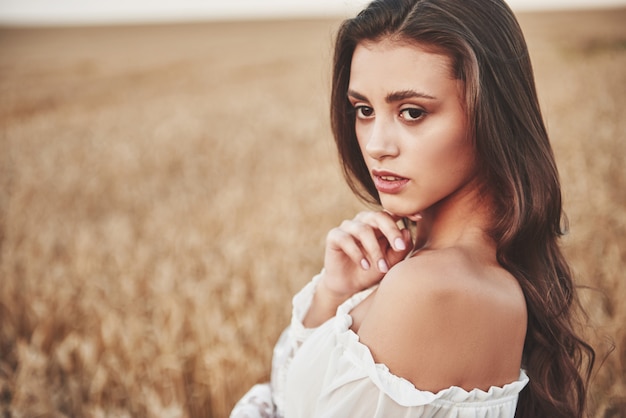 Retrato de una mujer feliz con el pelo largo que está en el campo de trigo