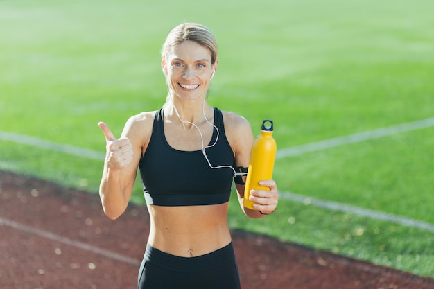 Retrato de mujer feliz en ropa deportiva rubia mirando a la cámara y mostrando los pulgares hacia arriba deportista en