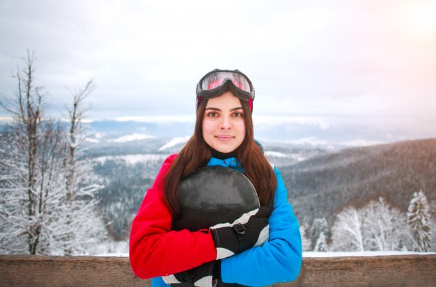 Retrato mujer feliz con snowboard en la cima de la montaña nevada