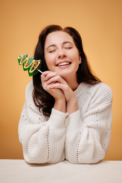 Retrato de mujer feliz sobre fondo amarillo con piruleta verde en forma de árbol de Navidad