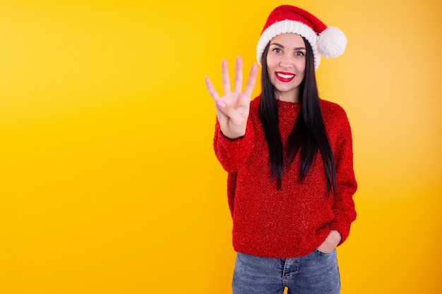 Retrato de mujer feliz y sonriente con sombrero de santa de Navidad, mostrando cuatro dedos.