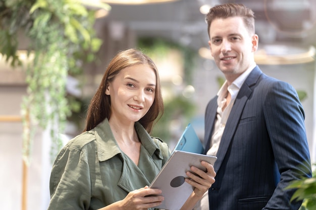 Retrato de una mujer feliz sosteniendo un dispositivo de tableta y sentada en la barra de café con un colega de fondo Concepto de tiempo de café de negocios con tecnología inteligente trabajando