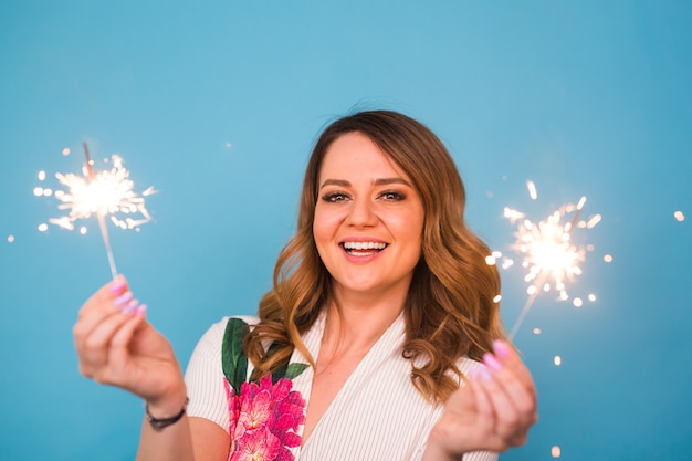 Retrato de una mujer feliz sosteniendo luces de bengala sobre fondo azul. Concepto de Navidad, celebraciones y vacaciones.