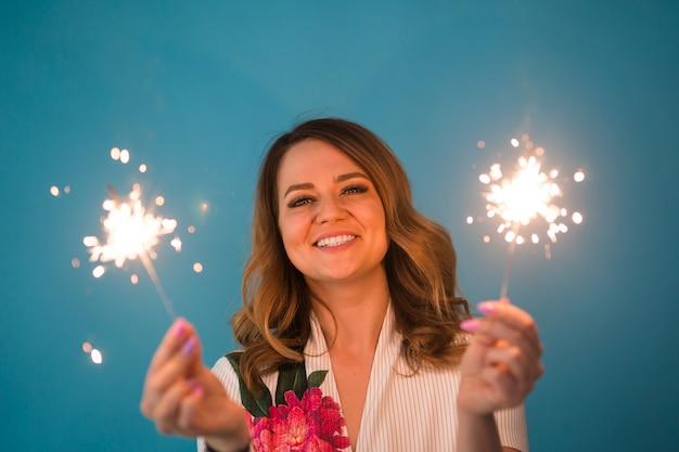 Retrato de una mujer feliz sosteniendo luces de bengala sobre fondo azul con espacio de copia. Concepto de Navidad, celebraciones y vacaciones.