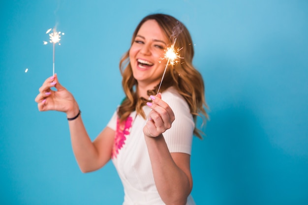 Retrato de una mujer feliz sosteniendo luces de bengala sobre fondo azul con espacio de copia. Concepto de Navidad, celebraciones y vacaciones.