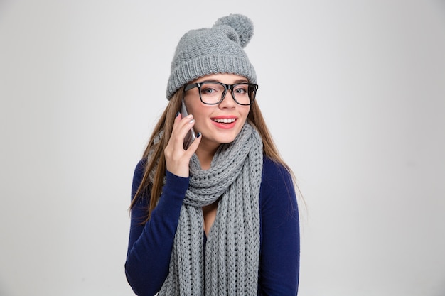 Retrato de una mujer feliz en tela de invierno hablando por teléfono y aislado en una pared blanca