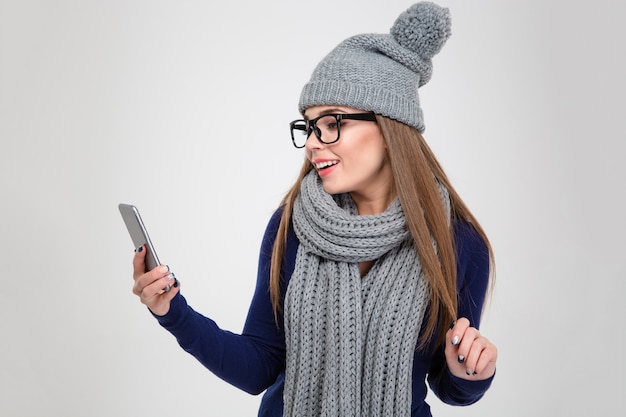 Retrato de una mujer feliz en tela de invierno con smartphone aislado en una pared blanca