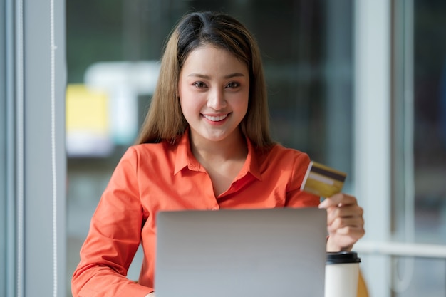 Retrato de mujer feliz usando laptop con tarjeta de crédito y rostro sonriente en oficina creativa o café en el centro comercial