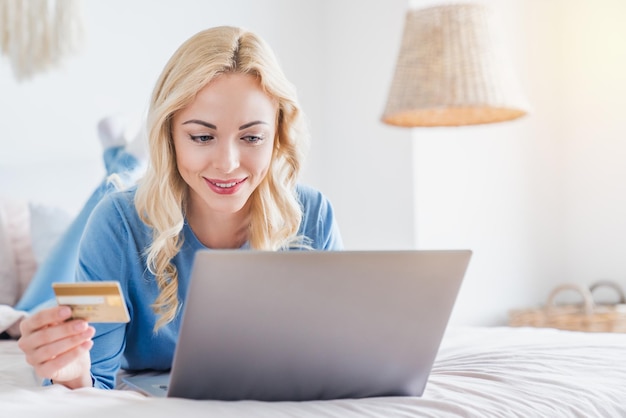 Retrato de una mujer feliz usando su tarjeta de crédito para comprar en línea con una laptop desde casa