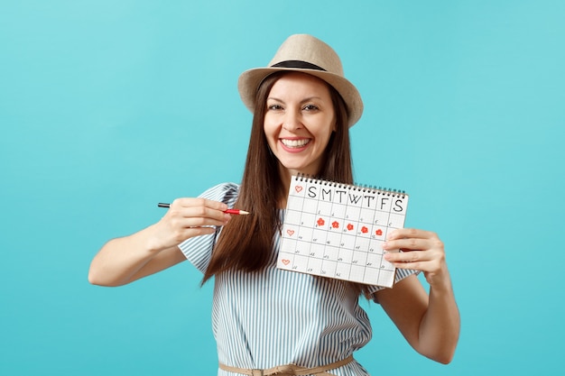 Retrato de mujer feliz en vestido azul, sombrero con lápiz rojo, calendario de períodos femeninos para comprobar los días de menstruación aislados sobre fondo azul. Atención médica, concepto ginecológico. Copia espacio