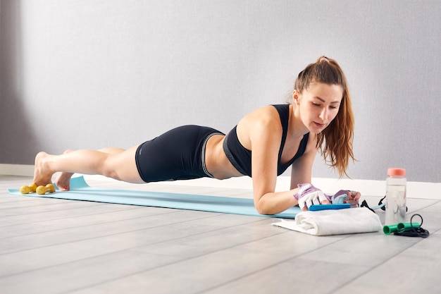 Retrato de mujer fitness aprendiendo ejercicios viendo tutoriales de entrenamiento en línea en su teléfono en casa