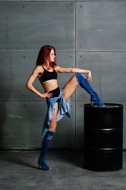 Retrato de mujer fitness en estudio sobre muro de hormigón de cemento, cerca de un barril negro.