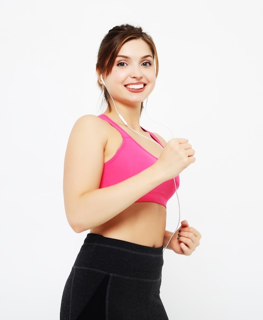 Retrato de una mujer fitness sonriente en auriculares trabajando aislado sobre fondo blanco.