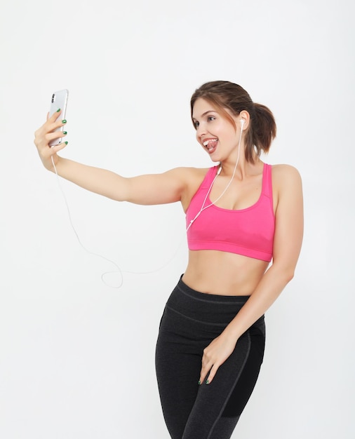 Retrato de una mujer fitness sonriente con smartphone Selfie tiempo sobre fondo blanco.