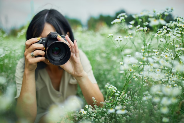 Retrato de mujer fotógrafa tomar fotos al aire libre en el paisaje de campo de flores sosteniendo una cámara, mujer mantenga cámara digital en sus manos. Fotografía de naturaleza de viajes, espacio para texto, vista superior.