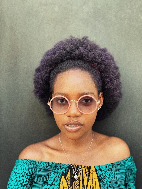 Retrato de una mujer con gafas de pie junto a la pared