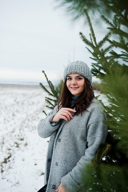Retrato de mujer gentil en abrigo gris y sombrero contra el árbol de Navidad al aire libre.